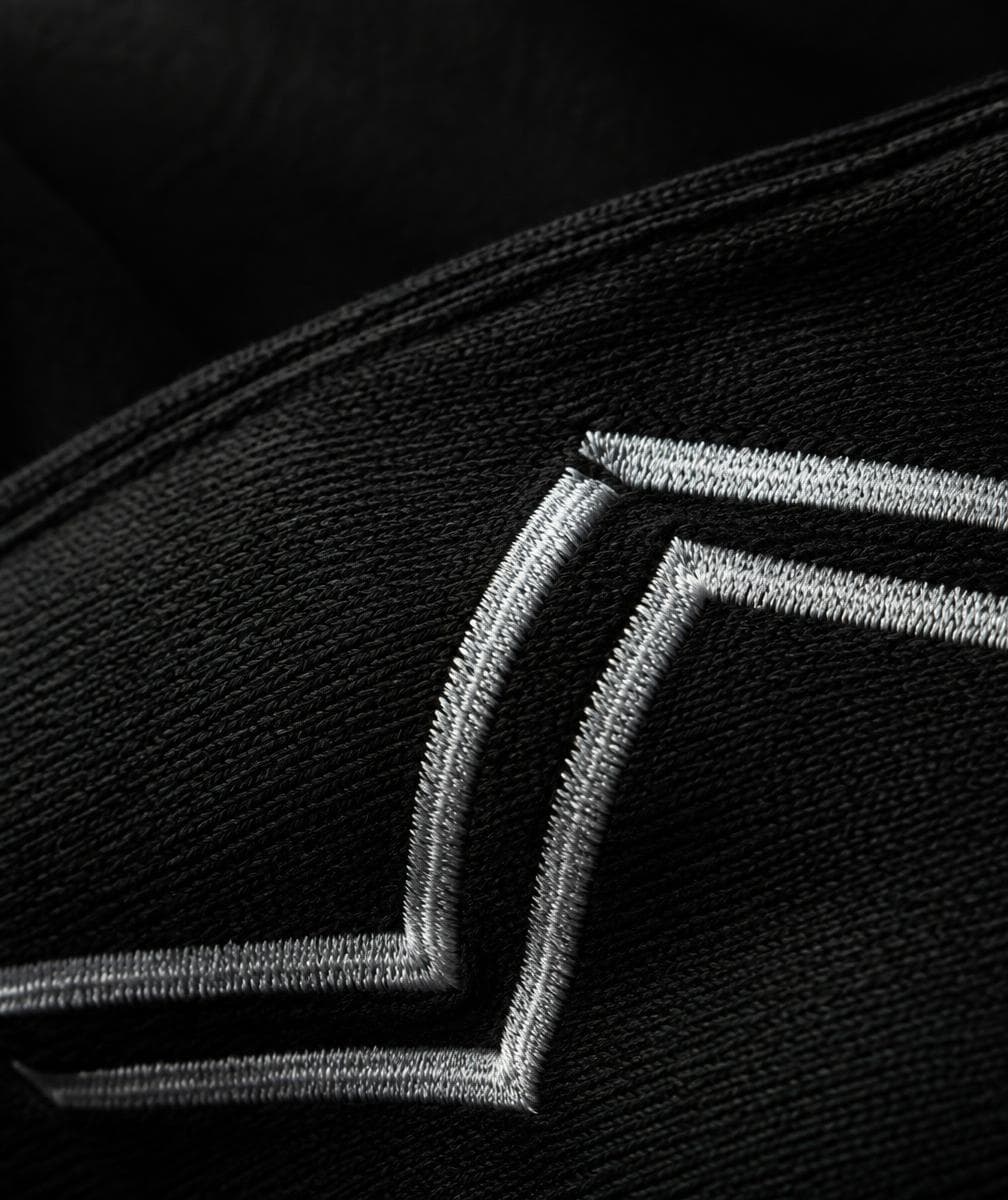 Close-up of the silver SYPIKE chevron embroidered on black heavyweight cotton